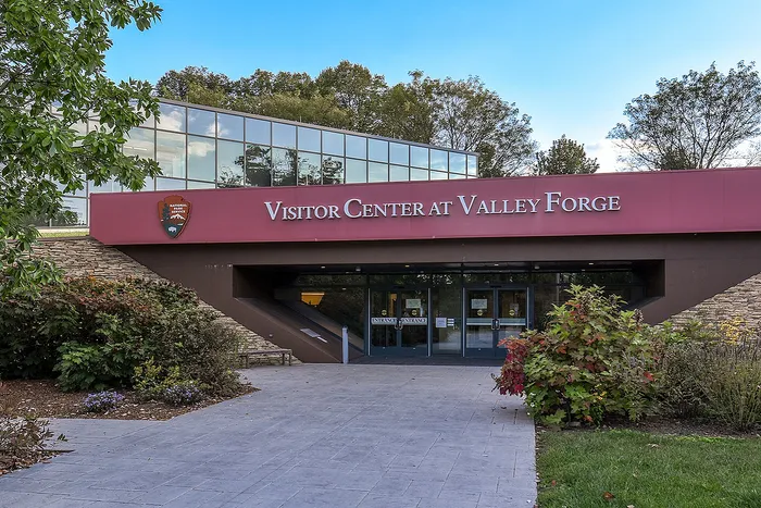 Modern visitor center at Valley Forge with expansive glass design, nestled among lush greenery and vibrant landscaping.