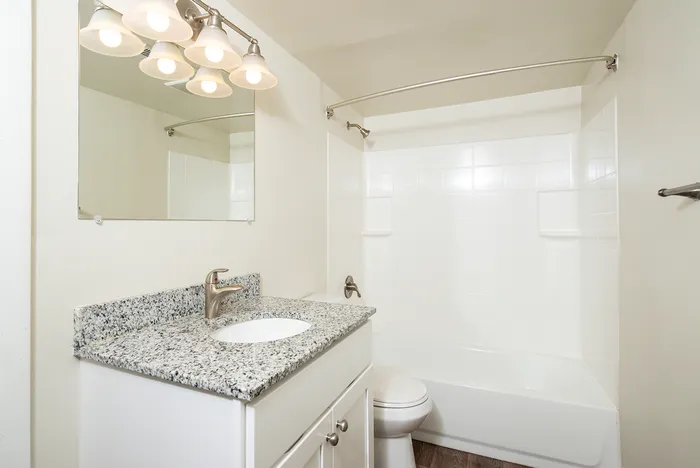 Bright and modern bathroom featuring a sleek granite countertop, elegant lighting, and pristine white tiles.