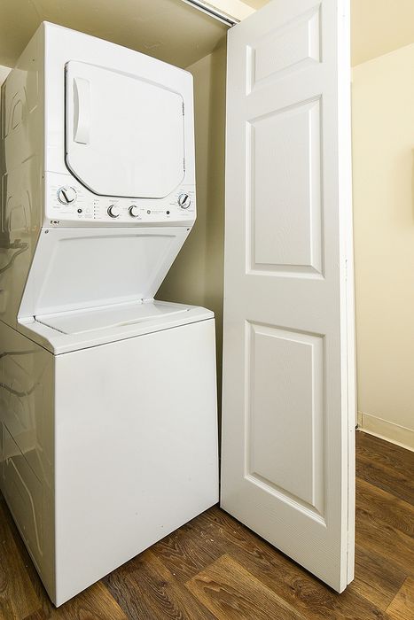 Modern apartment feature with an efficient stacked washer and dryer setup, complemented by elegant wooden flooring.