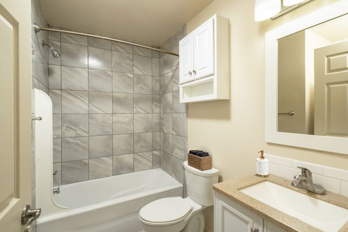 Bright and modern bathroom featuring elegant gray tile, a sleek vanity, and ample cabinet storage.