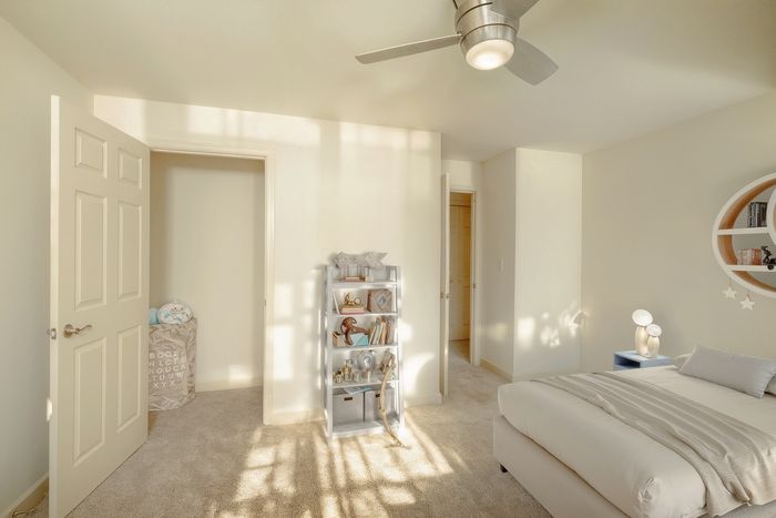 Bright and modern bedroom with cozy carpet, sleek shelving, and elegant ceiling fan, perfect for a serene retreat.