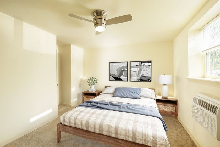 Inviting bedroom with a cozy bed, modern ceiling fan, and large window letting in natural light, perfect for relaxation.