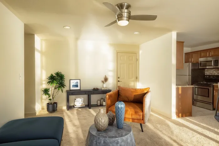 Inviting living space featuring a modern ceiling fan, cozy armchair, elegant decor, and an open view into a stylish kitchen.