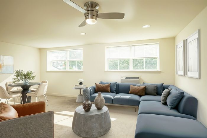 Bright and inviting lounge with a plush blue sectional, modern ceiling fan, and chic decor. Ideal for relaxation and entertaining.