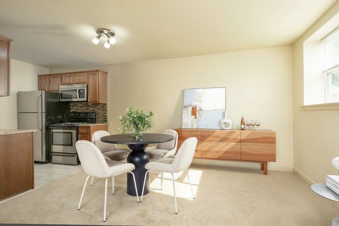 Bright and modern dining area with stylish round table, elegant chairs, and a sleek kitchen featuring stainless steel appliances.