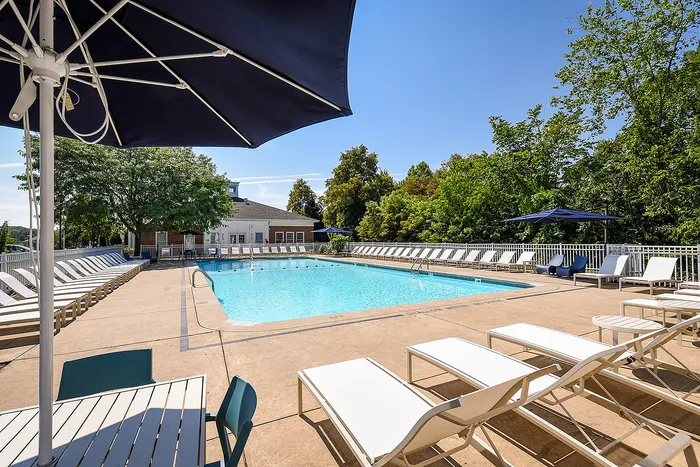 Inviting outdoor pool area with sun loungers, umbrellas, and lush greenery, perfect for relaxation on a sunny day.