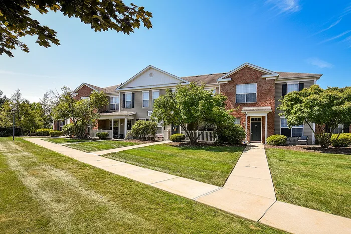 Charming townhouse complex with a vibrant brick facade, surrounded by lush greenery and a sunny blue sky, offering a welcoming and serene atmosphere.