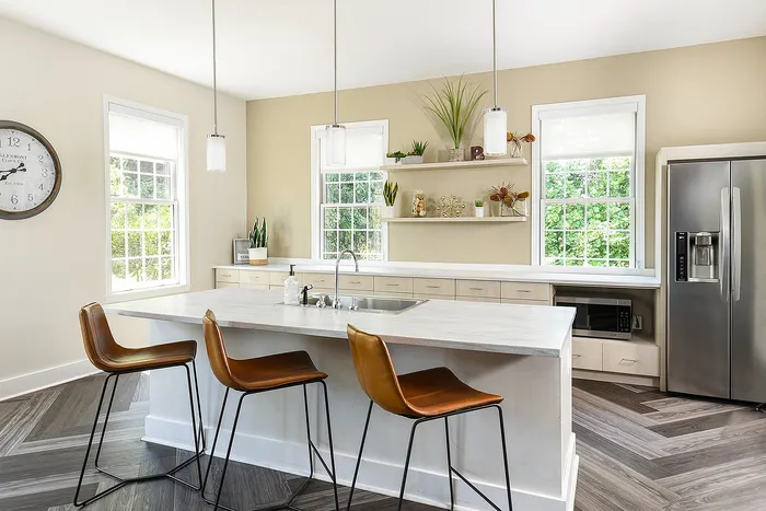 Bright and inviting modern kitchen with sleek countertops, stylish pendant lighting, and elegant bar stools against a backdrop of large windows and stainless steel appliances.