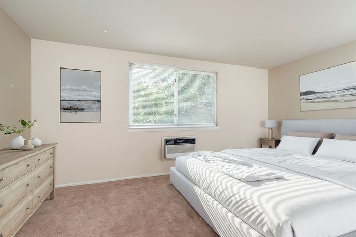 Bright and inviting bedroom with large window, cozy beige carpet, and elegant decor, featuring a plush king-sized bed for ultimate relaxation.