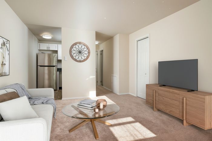 Bright and inviting living room with a modern design, featuring a cozy sofa, glass coffee table, and sleek TV stand, leading into a compact kitchen area.