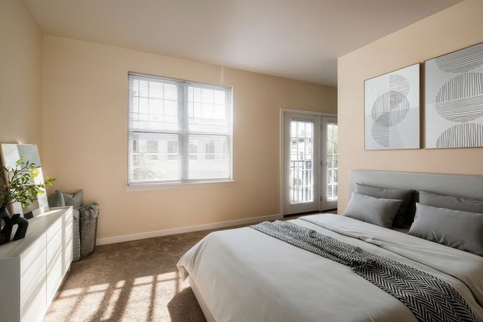 Bright, inviting bedroom with a modern design, featuring a large window, stylish artwork, and a cozy bed with elegant linens.