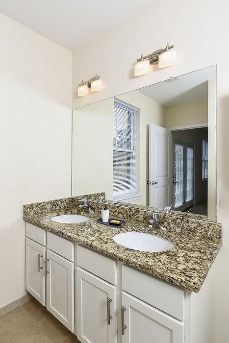 Elegant bathroom design featuring dual sinks with granite countertops, stylish lighting, and a large mirror.