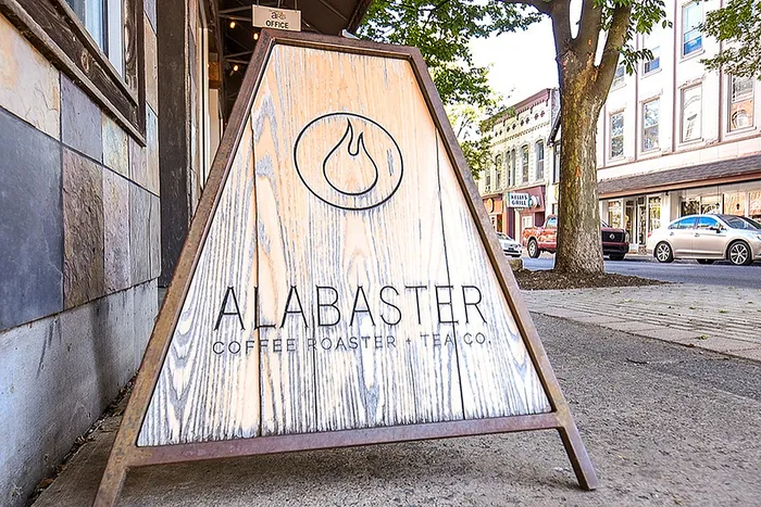Charming street sign of Alabaster Coffee Roaster & Tea Co. on a sunny, tree-lined downtown street, inviting and cozy ambiance.