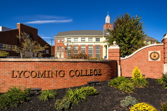 Welcoming entrance of a prestigious college with a beautiful red-brick building and manicured greenery under a clear blue sky.