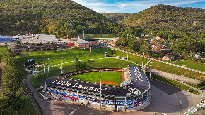 Impressive aerial view of a Little League stadium surrounded by lush greenery and scenic hills, perfect for sporting events and family gatherings.