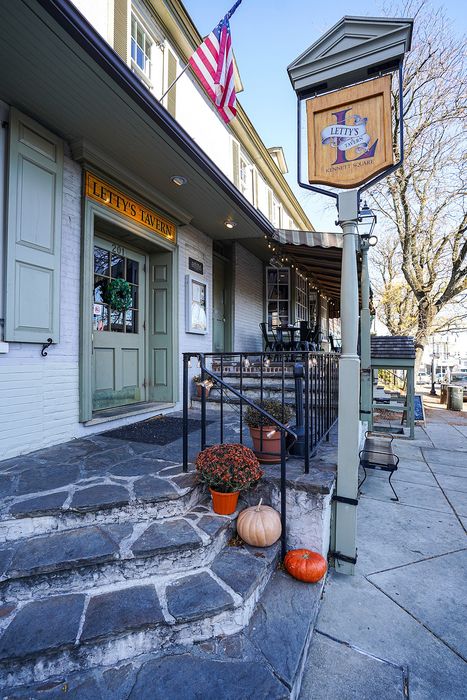 Charming exterior of Letty's Tavern with inviting wooden sign, cozy seating area, and seasonal decorations on a quaint stone pathway.