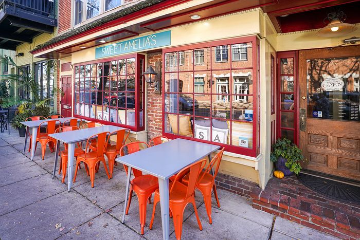 Charming corner cafe with vibrant orange chairs and tables set outside, inviting you to enjoy a delightful outdoor dining experience.