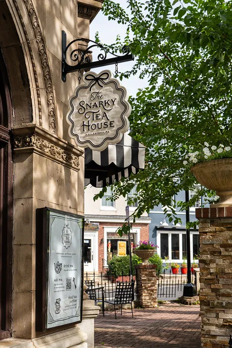 Charming Snarky Tea House entrance with ornate signage and inviting outdoor seating area, surrounded by lush greenery and classic architecture.