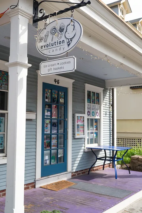 Charming storefront of Evolution Candy with inviting signage offering ice cream, cookies, and gift baskets on a sunny afternoon.
