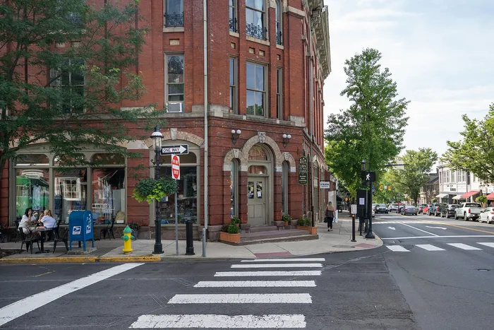 Charming street corner with a historic red-brick building, quaint outdoor cafe seating, and lush greenery, capturing a vibrant urban lifestyle.