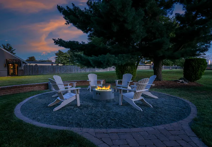 Inviting outdoor space with cozy Adirondack chairs and a central fire pit, nestled under a lush tree at sunset.