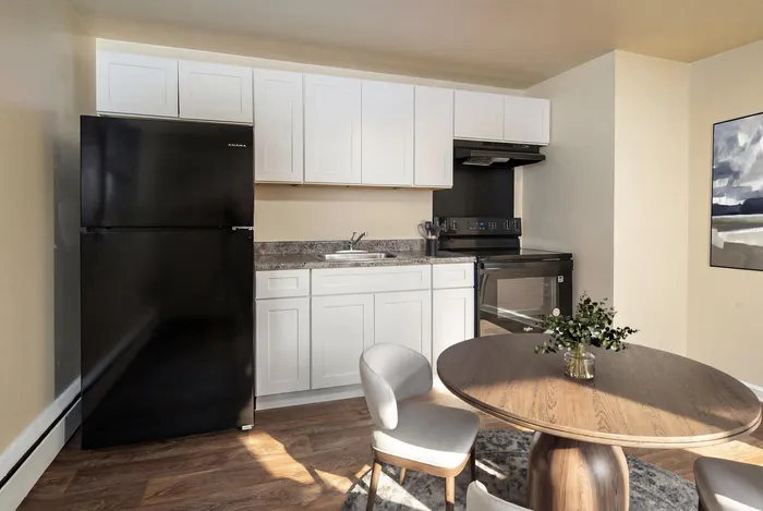 Charming kitchen with sleek black appliances, elegant white cabinetry, and a cozy dining area, perfect for modern living.