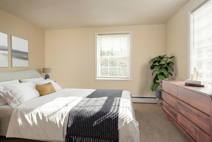 Sunlit bedroom with cozy bedding, elegant wooden dresser, and a lush green plant, perfect for relaxation.