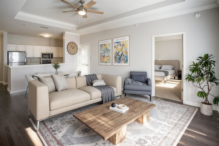 Chic open-plan living area with modern kitchen, cozy beige couch, stylish wooden coffee table, and inviting bedroom in view.
