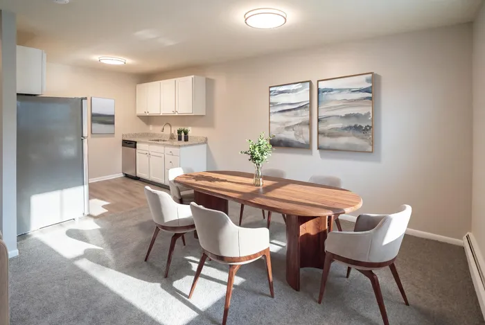 Bright and inviting dining area with a sleek wooden table, cushioned chairs, modern kitchen setup, and elegant wall art creating a cozy atmosphere.