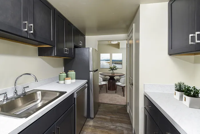 Modern kitchen with sleek dark cabinets, stainless steel appliances, and elegant countertops leading to a cozy dining area with scenic artwork.