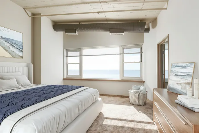Inviting bedroom with ocean view through large windows, featuring a cozy bed with elegant bedding and tasteful beach-themed decor.