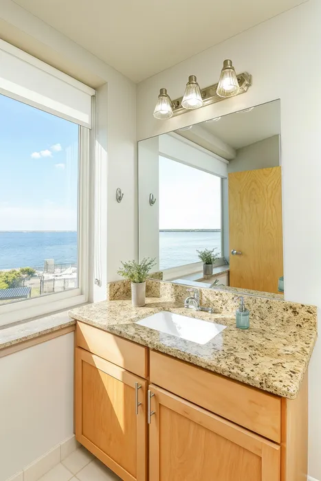 Bright and elegant bathroom with a granite countertop, large mirror, and stunning ocean view.