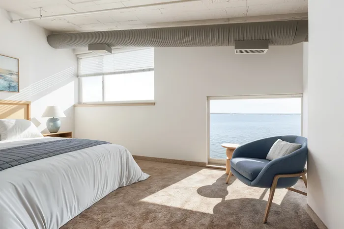 Serene bedroom with ocean views, featuring modern decor and cozy blue armchair.
