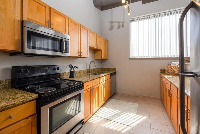 Beautifully lit kitchen with modern appliances, elegant wooden cabinetry, and sleek granite countertops, offering a warm and inviting cooking space.