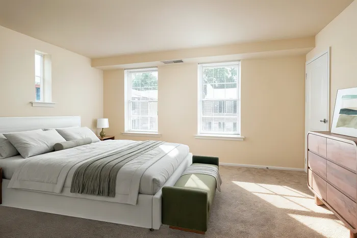 Bright and inviting bedroom with a large bed, elegant dresser, and natural light streaming through two windows.