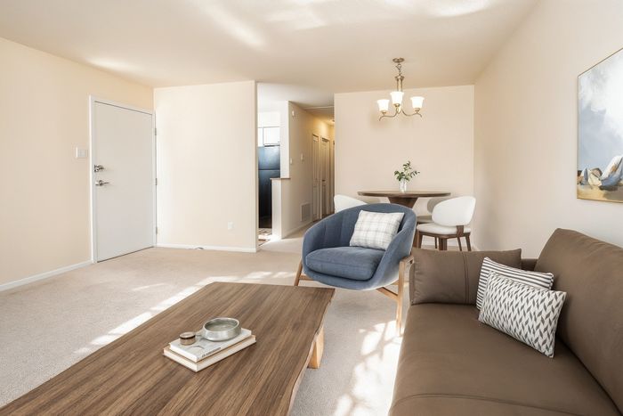 Bright and inviting living room with modern decor, featuring a comfortable sofa, stylish armchair, and elegant dining area under a chic chandelier.