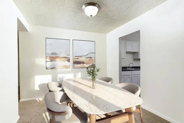 Inviting dining area with a chic marble table, elegant chairs, and modern art, leading to a sleek kitchen.