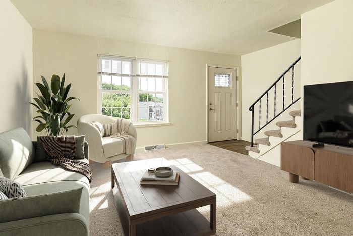 Inviting living room with plush carpet, modern furniture, and abundant natural light streaming through large windows, complemented by a cozy staircase.