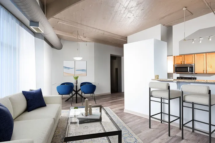Modern loft-style apartment featuring an open-concept layout with a cozy living area, stylish kitchen with wooden cabinets, and elegant dining space with sleek blue chairs.