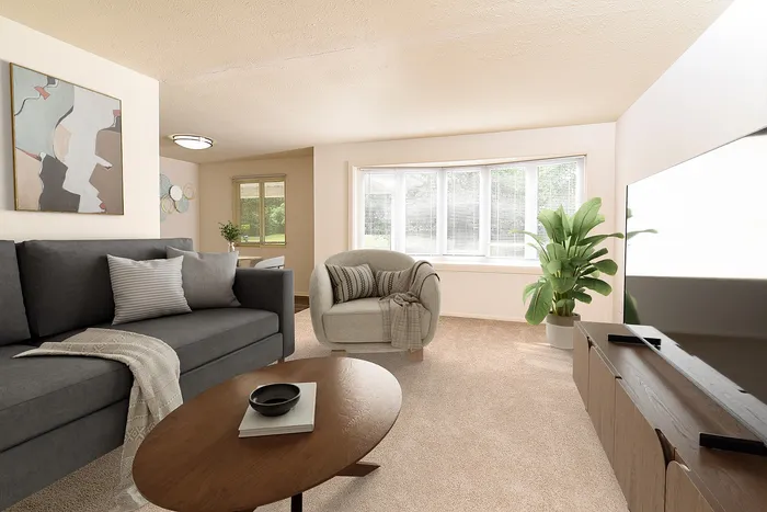 Bright and inviting living room with a cozy gray sofa, modern decor, and large windows overlooking greenery.