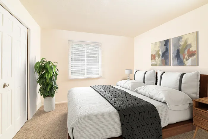Inviting bedroom with a plush bed, elegant artwork, and natural light from a large window, complemented by a chic potted plant.