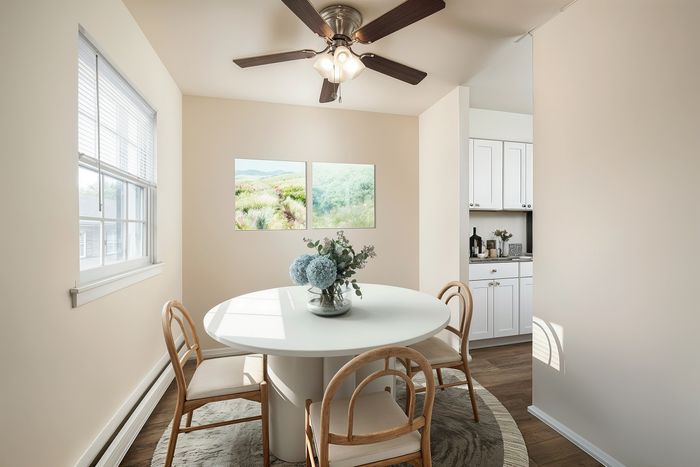 Bright dining area featuring a round white table with elegant chairs, accented by fresh blue hydrangeas and modern artwork, adjacent to a sleek kitchen with white cabinets.