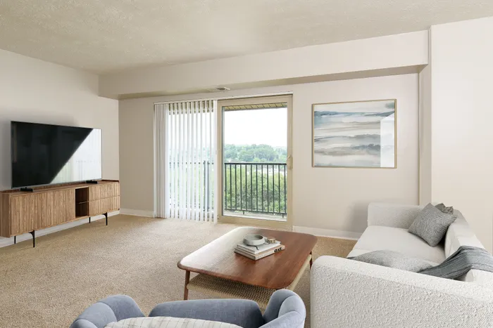 Bright and inviting living room with a modern sofa, large flat-screen TV, and a beautiful view through glass doors leading to a balcony, perfect for relaxation.