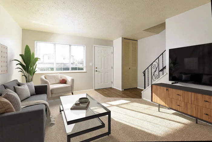 Bright living room with modern decor featuring a cozy gray sofa, stylish armchair, and large flat-screen TV beside an elegant staircase.