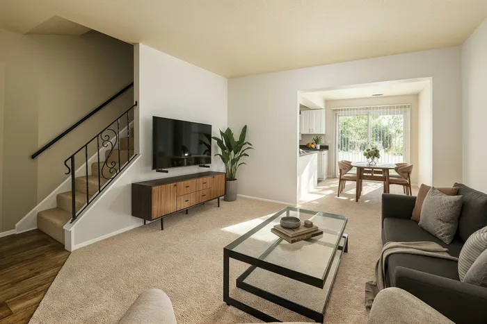 Inviting living room with modern staircase, sleek TV setup, cozy gray sofa, and bright dining area with garden view.