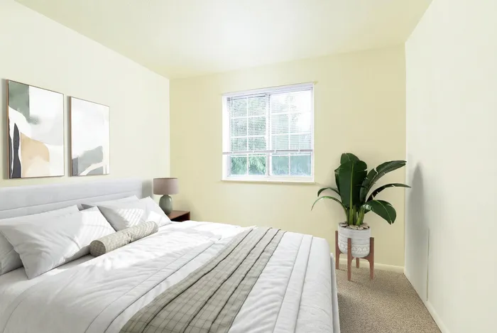 Sunlit bedroom with cozy bed, modern artwork, and a lush green plant for a serene atmosphere.