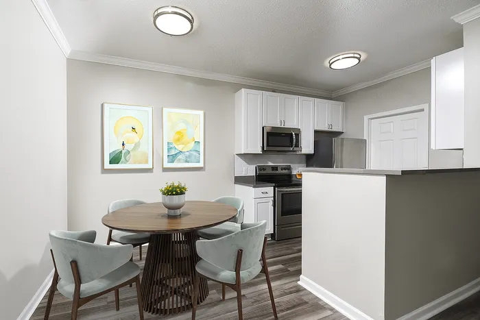 Modern kitchen and dining area with sleek white cabinets, stainless steel appliances, and a chic circular table complemented by stylish art decor.