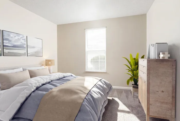Bright and inviting bedroom featuring a cozy bed with beige and blue bedding, a sunlit window with blinds, tasteful wall art, a sleek wooden dresser, and a vibrant green plant.