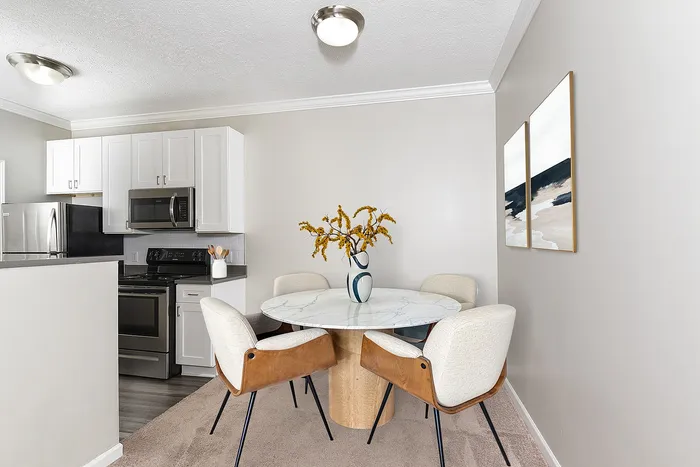 Chic dining area with a marble-top table and elegant upholstered chairs, adjacent to a modern kitchen with stainless steel appliances.