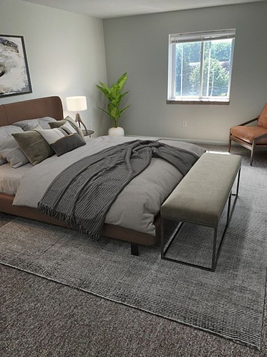 Elegant bedroom featuring a large bed with cozy gray bedding, stylish bench, and modern decor with natural light enhancing the serene ambiance.